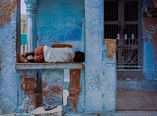 Một bé trai nằm ngủ ngay trước ngôi nhà được sơn màu xanh.