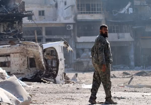 Một binh sĩ Syria đứng trước tòa nhà bị hư hại ở khu vực Ramouseh.