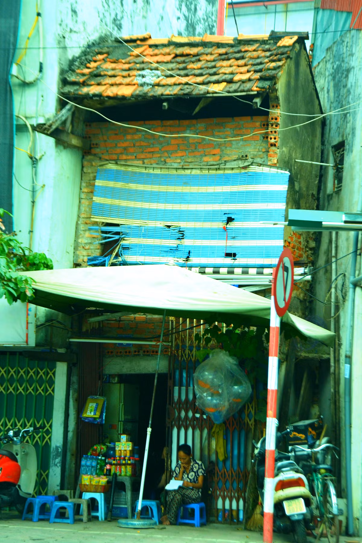 Một ngôi nhà mái ngói 2 tầng lụp xụp, lộ ra với vẻ lem nhem, chắp vá lọt thỏm giữa những ngôi nhà cao tầng.