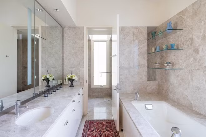 Phòng tắm ốp đá cẩm thạch sáng với hệ tủ có cánh cửa kính giúp không gian rộng hơn.