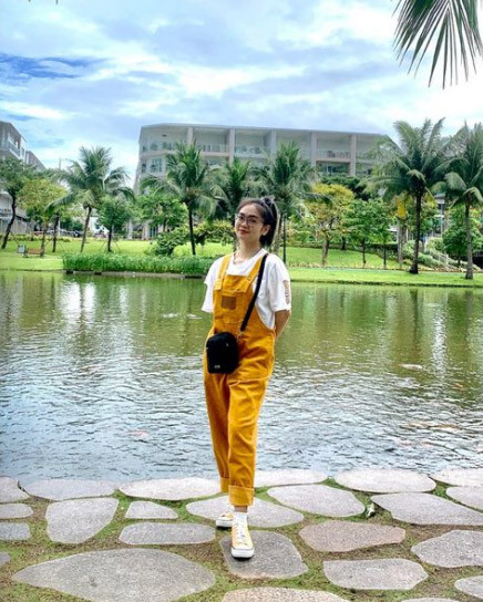 Thiện Nhân nhí nhảnh với set quần yếm vàng, áo phông trắng, giày sneaker.