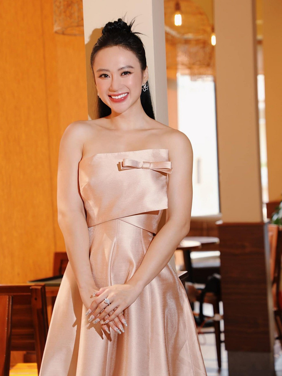 Angela Phương Trinh mặc bộ váy hồng pastel nhẹ nhàng, kết hợp trang sức điệu đà, để lộ vai và tay trong một buổi đi phỏng vấn.