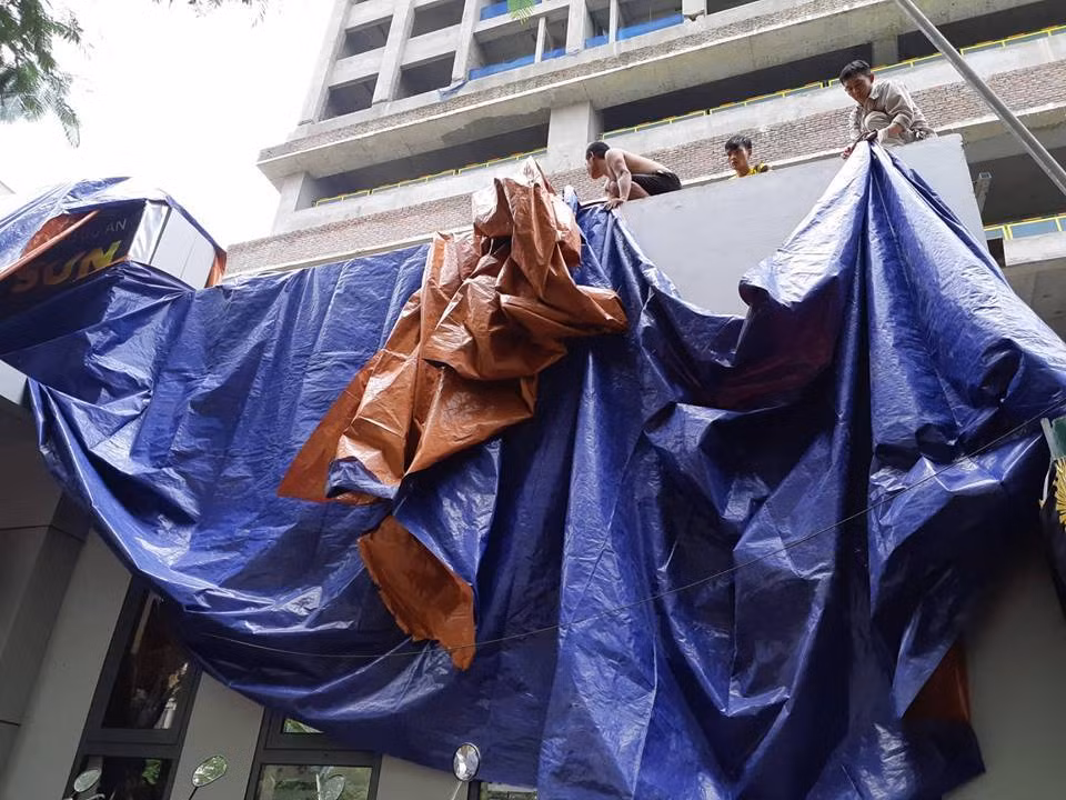 Trong khi đó, các công nhân tại đây khẩn trương sử dụng bạt phủ kín hiện trường.