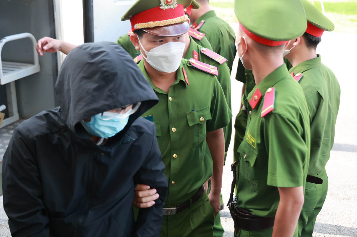 Một bị cáo mặc áo kín đầu, đeo khẩu trang khi bước xuống từ xe đặc chủng.