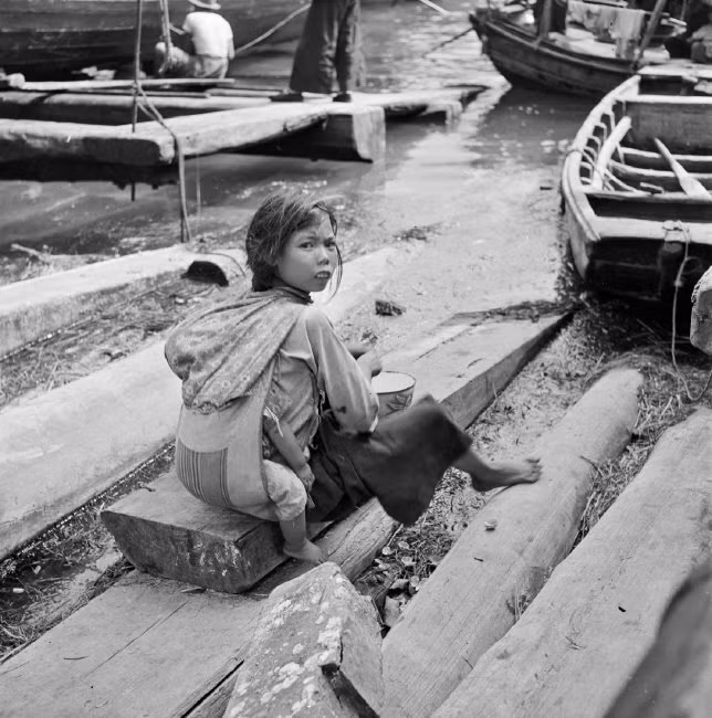 Bé gái địu em trên lưng, ăn bữa trưa ở bến thuyền. Ảnh: Werner Bischof/ Magnum Photos.