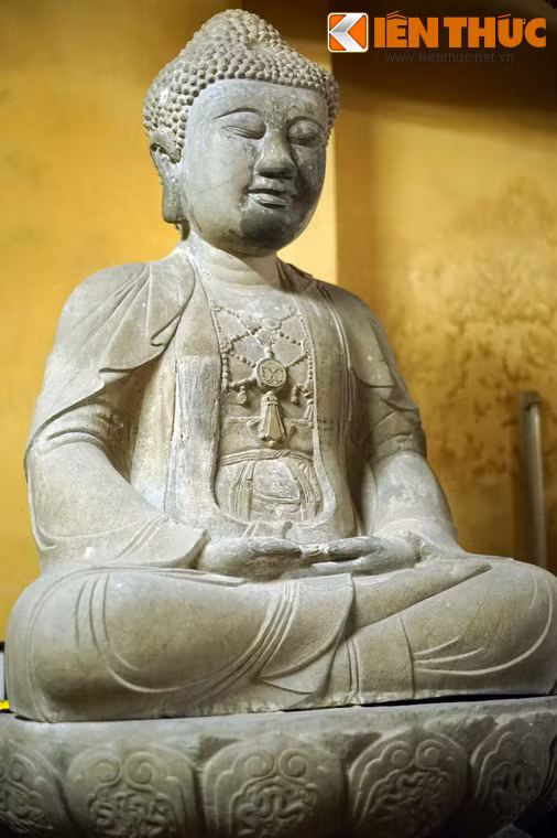 Bức tượng bên trái khác hai pho kia trong tư thế ngồi thiền, với hai tay để nhẹ nhàng trên đùi kết ấn “ tam muội”. Áo tượng cũng có ba lớp với những điểm khác biệt dễ nhận ra về họa tiết trên ngực.