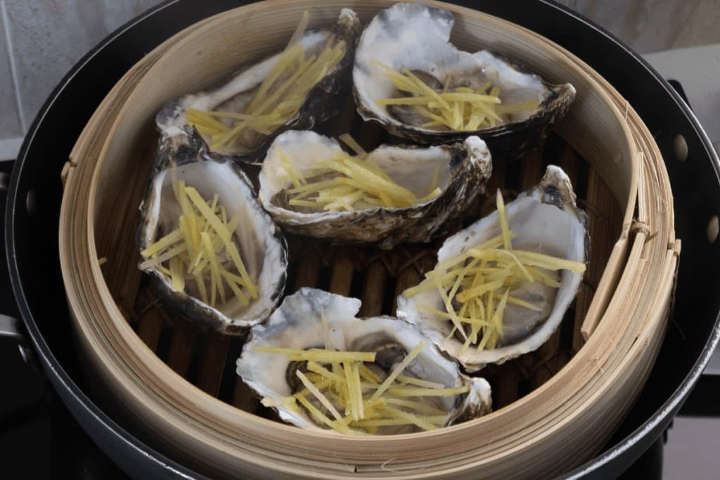  Hàu hấp gừng: 5 con hàu tươi loại lớn, gừng tươi, hành lá, ớt sừng, rau răm, nửa củ cà rốt, gia vị. Sơ chế hàu, bỏ phần vỏ trên. Đập giập tiêu sọ vừa nát. Cạo vỏ gừng, rửa sạch, thái sợi chỉ. Hành lá, ớt, cà rốt, thái sợi chỉ. Trộn đều gừng, hành lá, ớt sừng, bột nêm, tiêu sọ, dầu hào. Cho hỗn hợp này lên hàu, hấp chín. Ảnh Internet