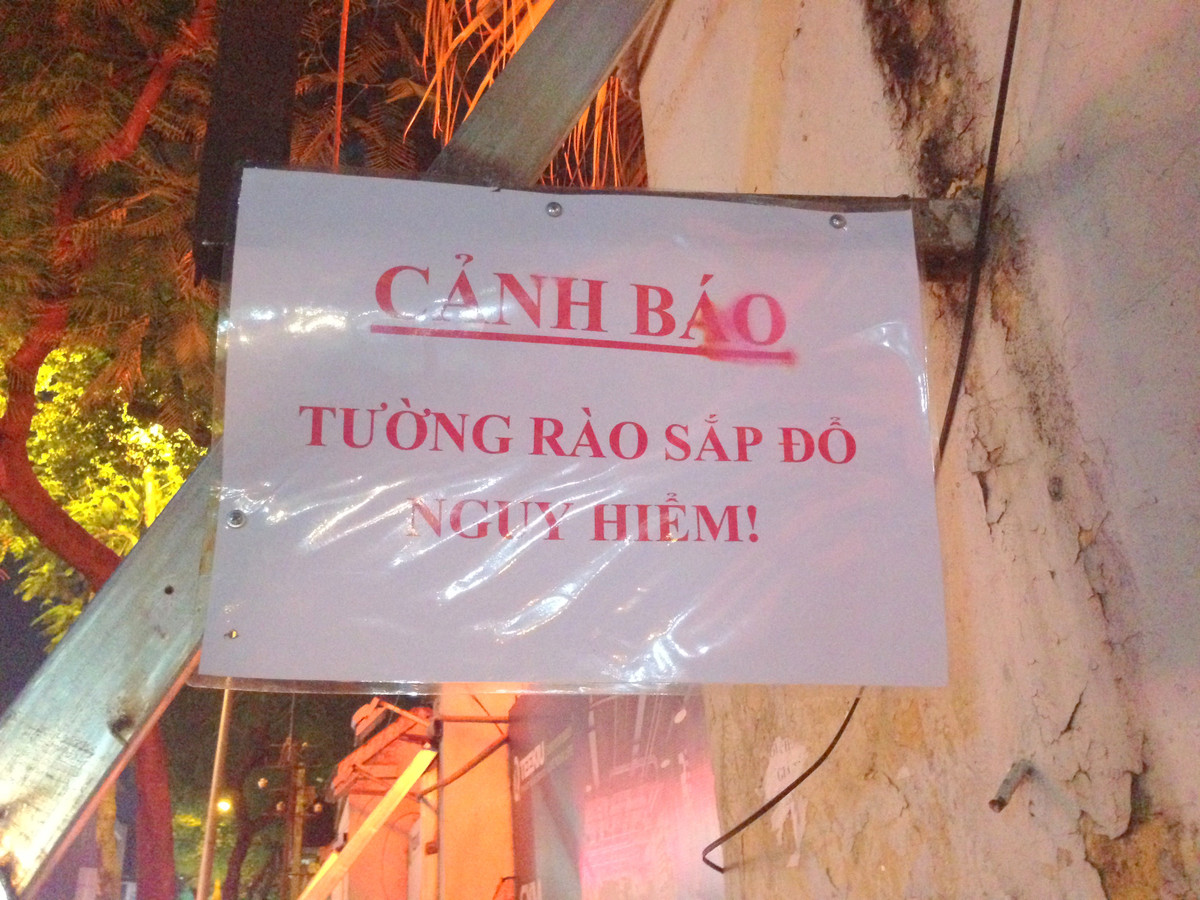 Biển cảnh báo nguy hiểm tường rào sắp đổ được dán hai bên đầu bức tường.