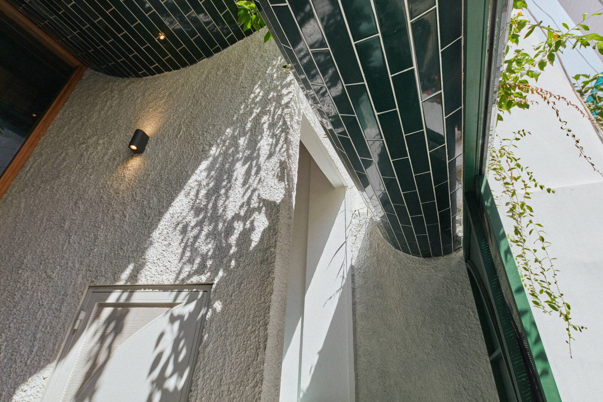 Gạch thẻ xanh vừa là điểm nhấn vừa tạo ra sự tương phản chất liệu với bức tường trắng xù xì và chất liệu bê tông thô của những mảng lam che nắng mặt tiền.