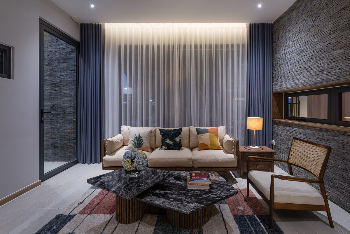 Ở giữa phòng khách là một bộ salon gỗ đệm tựa màu trắng ngà và bàn trà mặt đá đen sang trọng.