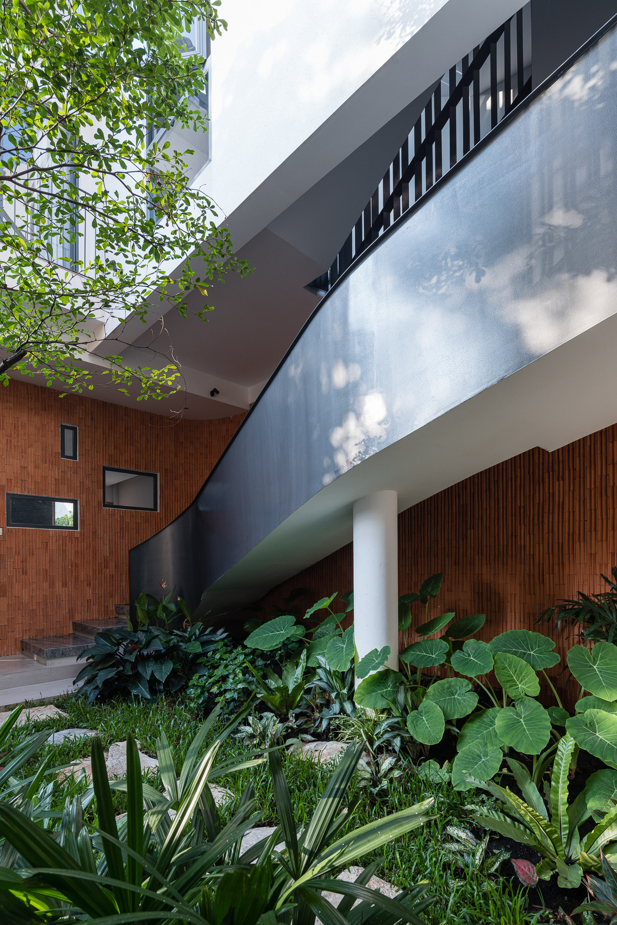 Bên cạnh phòng khách là một mảng vườn nhỏ nhiều cây xanh. Khoảng vườn xanh cũng làm nổi bật mảng tường gạch đỏ được ốp dọc theo chiếc thang xoắn hướng lên phòng bếp.