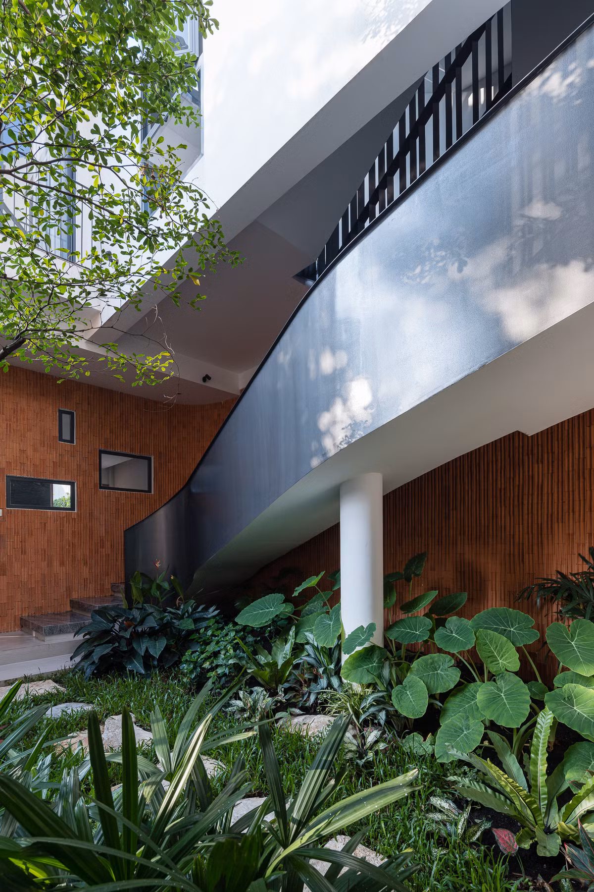 Bên cạnh phòng khách là một mảng vườn nhỏ nhiều cây xanh. Khoảng vườn xanh cũng làm nổi bật mảng tường gạch đỏ được ốp dọc theo chiếc thang xoắn hướng lên phòng bếp.