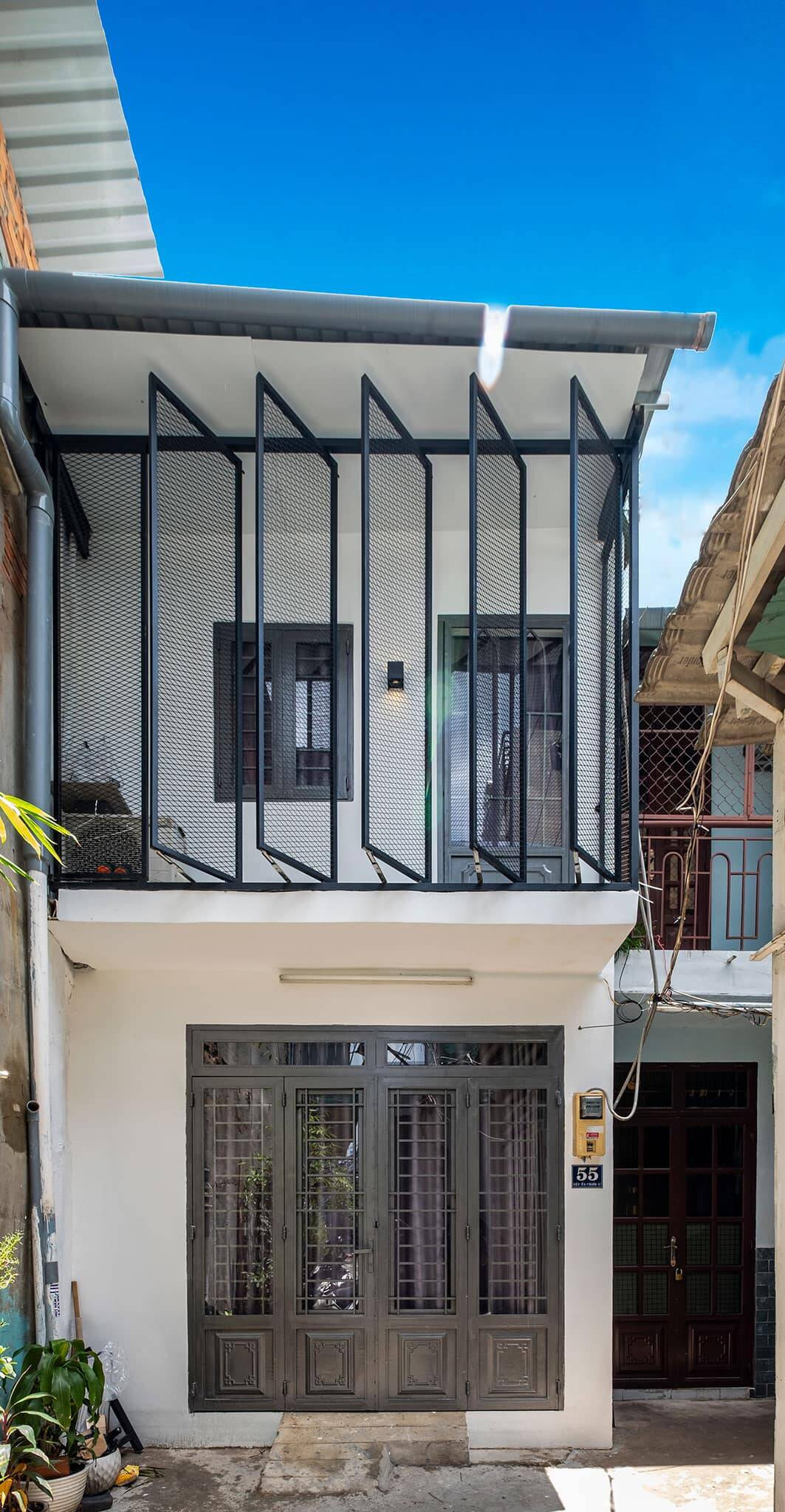 Sau cải tạo, ngôi nhà lột xác hoàn toàn với gam màu chủ đạo là trắng - đen cùng sơn hiệu ứng bê tông. Ban công tầng 2 được bố trí cửa khung sắt bật 45 độ vừa tạo điểm nhấn, vừa đảm bảo tính riêng tư. Ảnh: Happynest