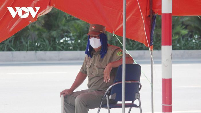 Đội khăn chống nắng, ghé tạm dưới ô trong ca trực, nhưng lực lượng dân phòng vẫn không rời chốt.