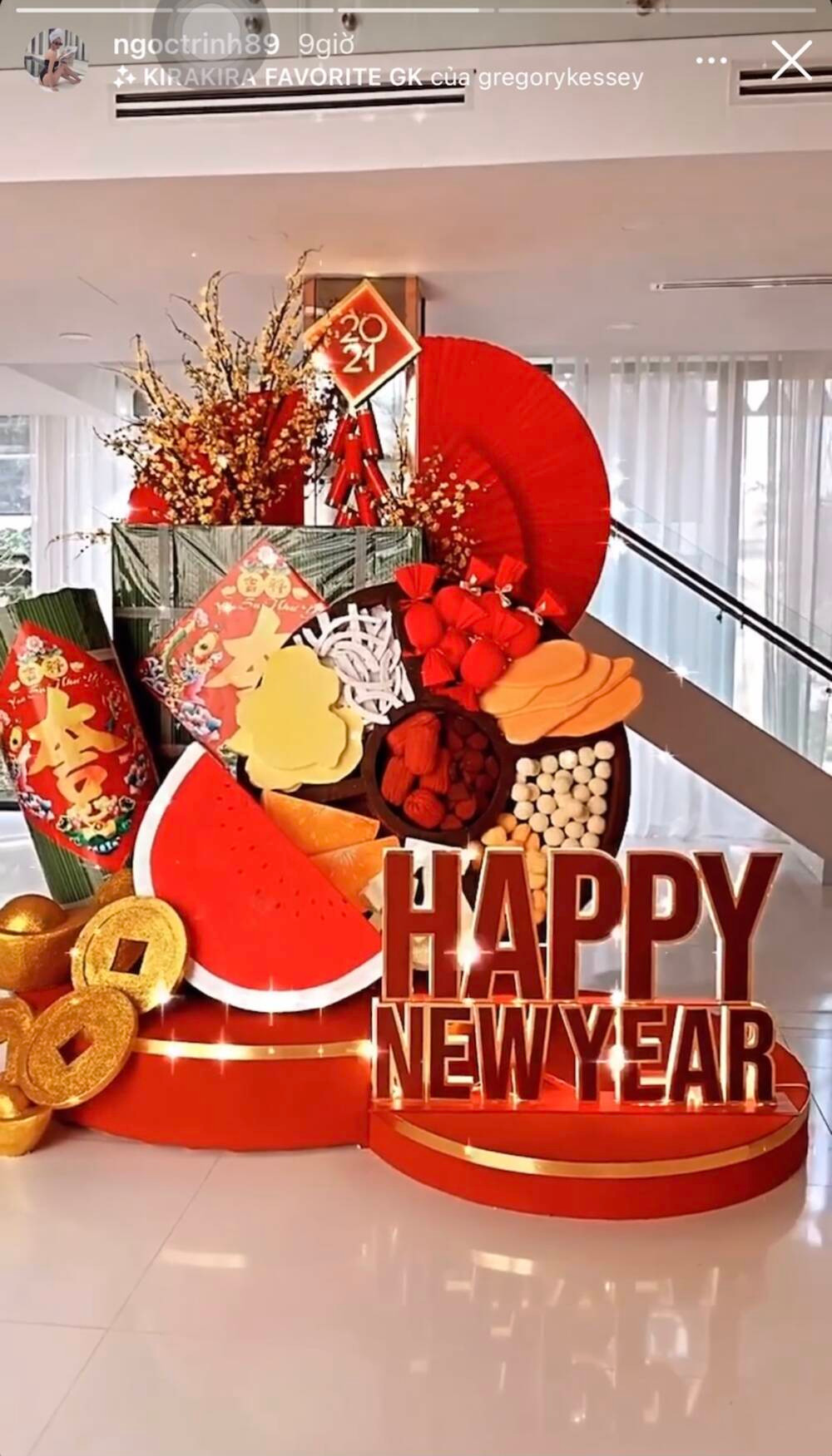 Giữa nhà là một mô hình khổng lồ với khung bánh mứt, bánh chưng, bánh tét, hoa mai, dưa hấu, đồng tiền và dòng chữ Happy New Year.