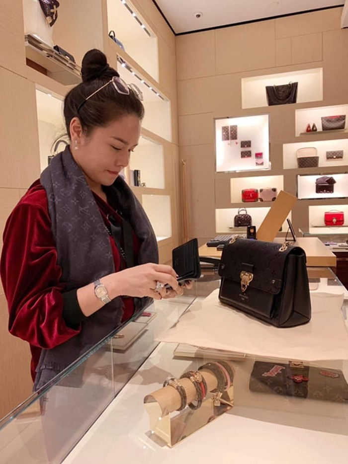 Nhật Kim Anh quàng khăn Louis Vuitton, xách túi Channel, tay đeo đồng hồ hiệu và nhẫn kim cương, mua sắm tại một cửa hàng Louis Vuitton.