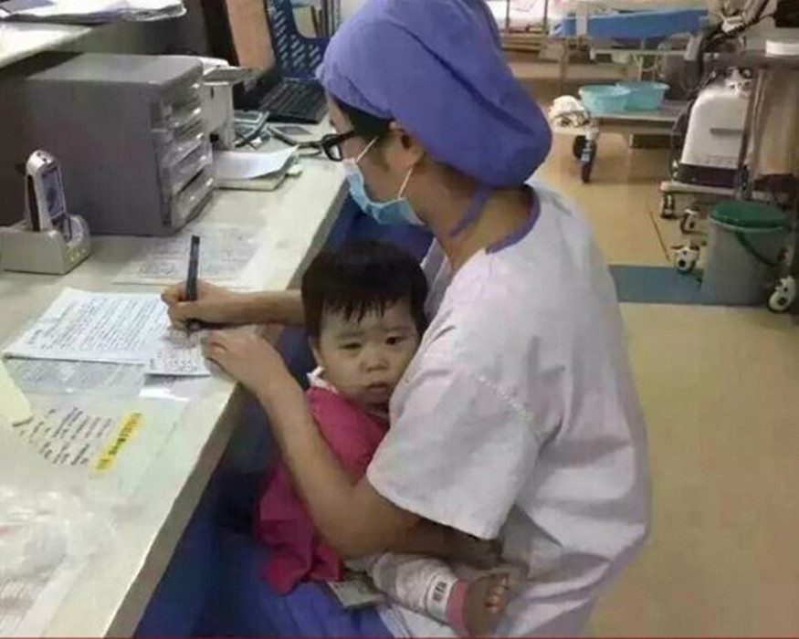 Bé gái trong phòng bệnh khóc và nhất định không chịu rời xa cô y tá. Nữ y tá này không đành lòng để đứa trẻ khóc, nên cô chỉ còn cách vừa bế đứa trẻ vừa làm việc.