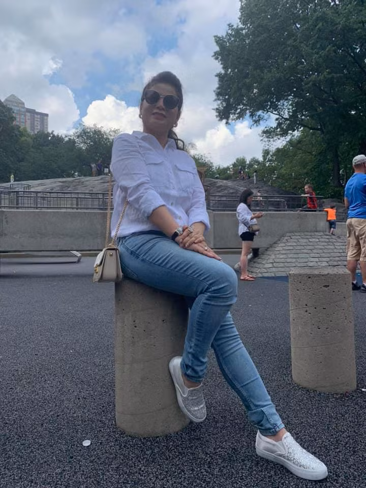 Bà diện quần jeans, áo sơ mi trắng trẻ trung, đi giầy thể thao tiệp màu với áo, phụ kiện đi kèm là kính mắt và túi xách nhỏ gọn.