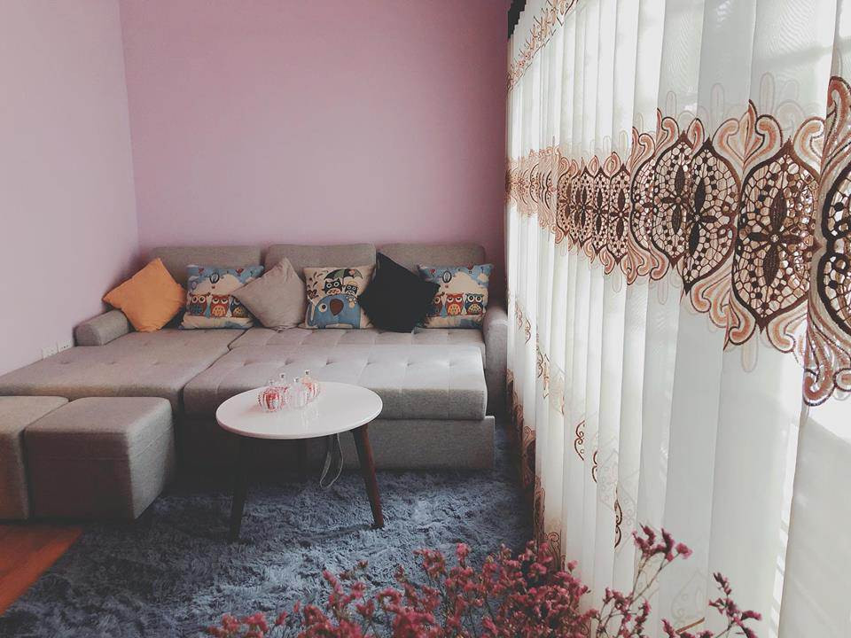 Căn phòng trang trí nhẹ nhàng với sofa xám, thảm lông và rèm vải mỏng.