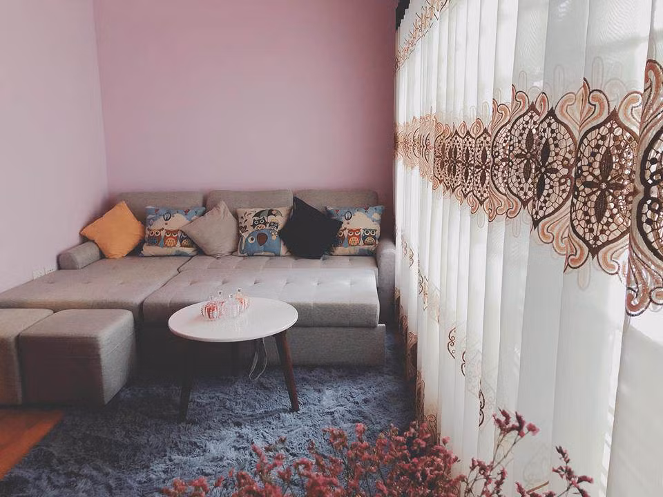 Căn phòng trang trí nhẹ nhàng với sofa xám, thảm lông và rèm vải mỏng.