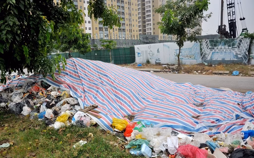 Ban quản lý tòa nhà dùng tấm bạt lớn nhưng chỉ phủ được một phần đống rác thải không di chuyển được do người dân chặn đường vào bãi rác Nam Sơn. Ảnh: Batdongsanvietnam.