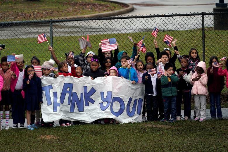 Các em nhỏ vẫy cờ và cầm băng rôn có dòng chữ “Cảm ơn” khi đoàn tàu chở linh cữu vị tổng thống thứ 41 của nước Mỹ đi qua.