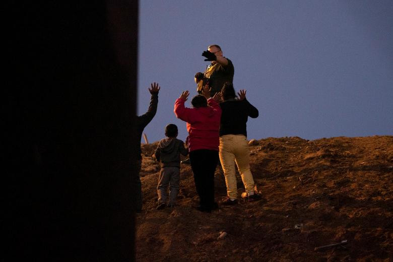 Một số di dân giơ tay đầu hàng trước lực lượng biên phòng Mỹ ở San Diego.