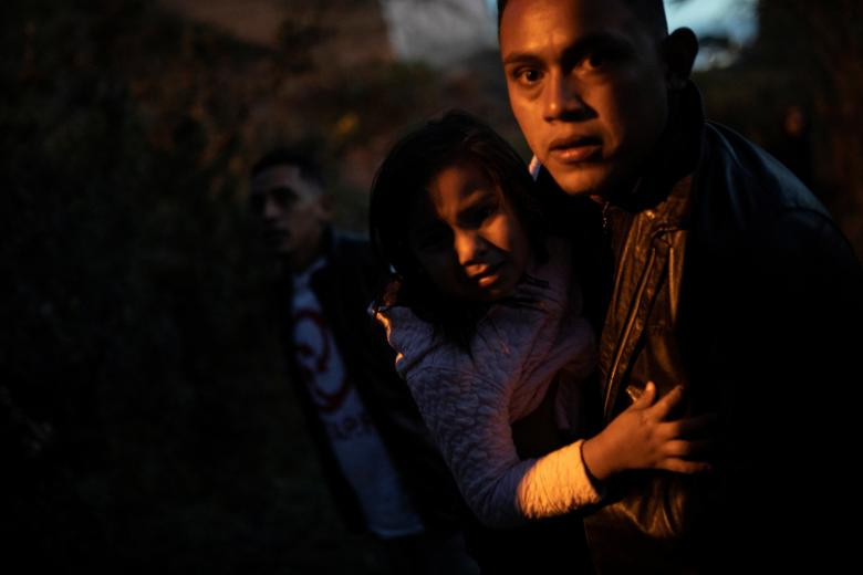 Người đàn ông đến từ Houduras bế một bé gái trong lúc tìm cách nhảy qua hàng rào biên giới để vượt biên trái phép từ Tijuana, Mexico, vào Mỹ hôm 2/12.