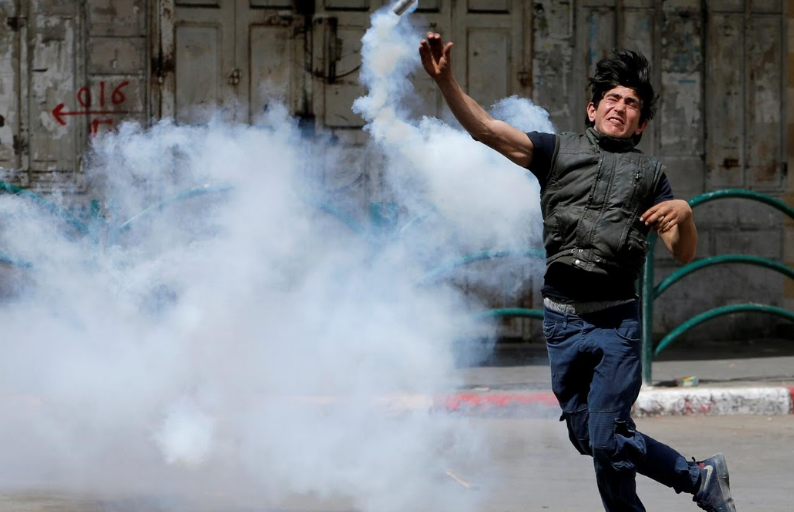 Một người biểu tình Palestine ném trả lựu đạn hơi cay về phía binh sĩ Israel tại Hebron.