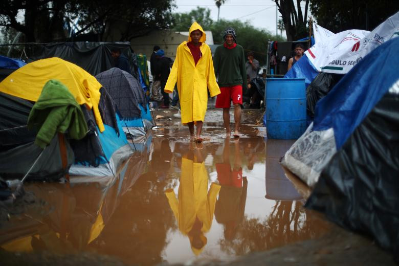 Một di dân mặc áo mưa đi bộ trong khu trại.