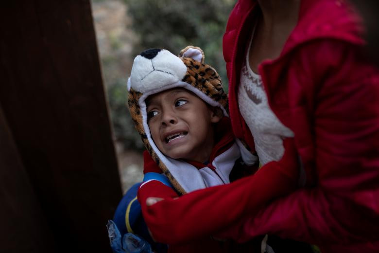 Một bé trai có vẻ sợ hãi khi nhìn mọi người cố trèo qua hàng rào biên giới. 