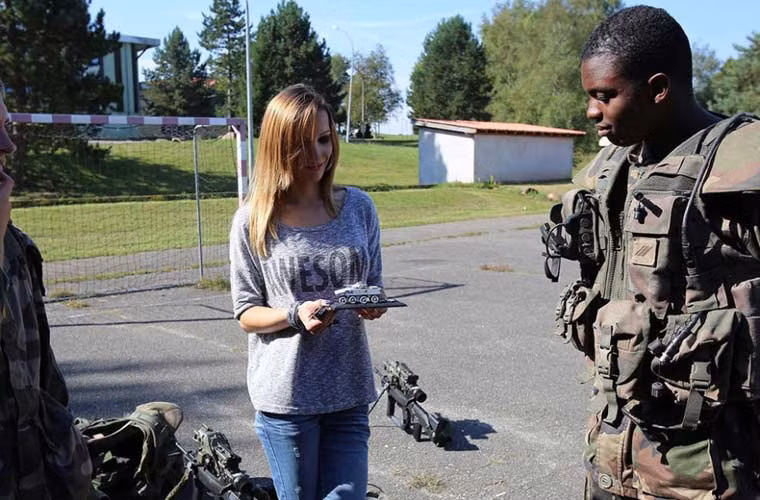 Cô gái trẻ tỏ ra thích thú khi nhận được món quà mô hình xe thiết giáp từ tay các binh sĩ Quân đội Pháp.