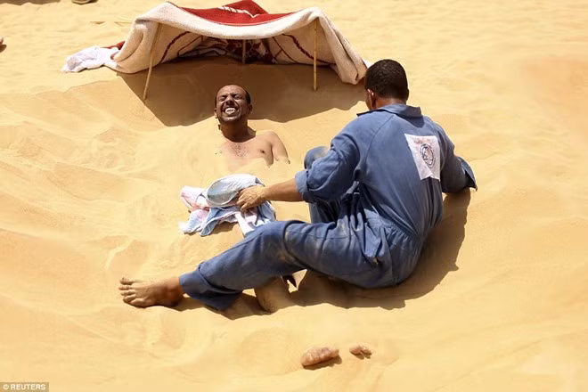 Một bệnh nhân nhăn mặt khi cát nóng phủ khắp cơ thể.