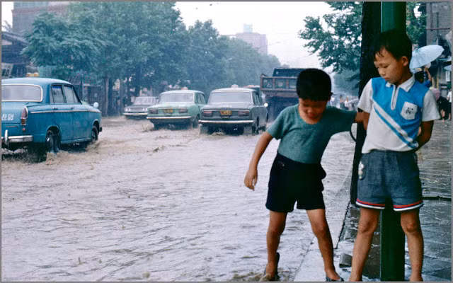 Hai bé trai đứng bên mép đường ngập lênh láng nước giữa lúc xe hơi đang lướt qua đoạn đường này. Ảnh VT