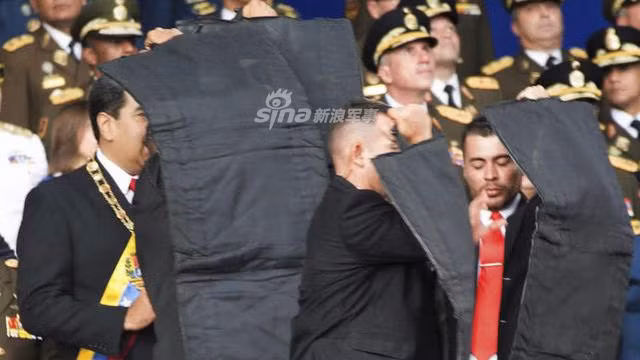 Sau đó, Tổng thống được ngay lập tức dẫn tới khu vực an toàn, lên xe và rút khỏi nơi xảy ra vụ việc. Do mục tiêu là một máy bay không người lái nên những cận vệ của ông Maduro hoàn toàn không rút súng ra sử dụng. Nguồn ảnh: Sina.