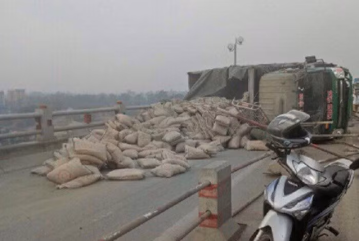 Tai nạn khiến những bao tải xi măng chở trên thùng xe tải bị rơi chắn ngang đường, dải phân cách phân làn phương tiện bị đâm lộn xộn, các phương tiện tham gia giao thông trên đường này bị chặn, khó di chuyển.