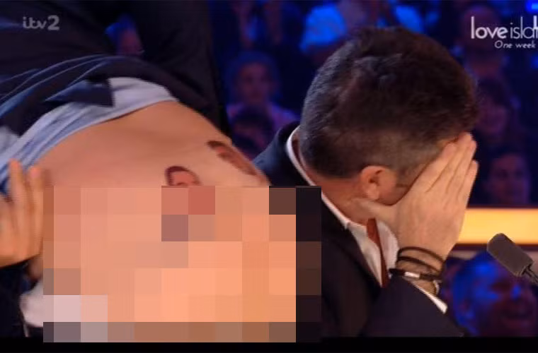 Trong khi David khoe hai hình xăm, một bên là hình ảnh của chính David, một bên là hình ảnh Simon Cowell và dòng chữ "Forever In Love", thì Simon lấy tay che mặt, quay đi chỗ khác. (Ảnh: ITV)