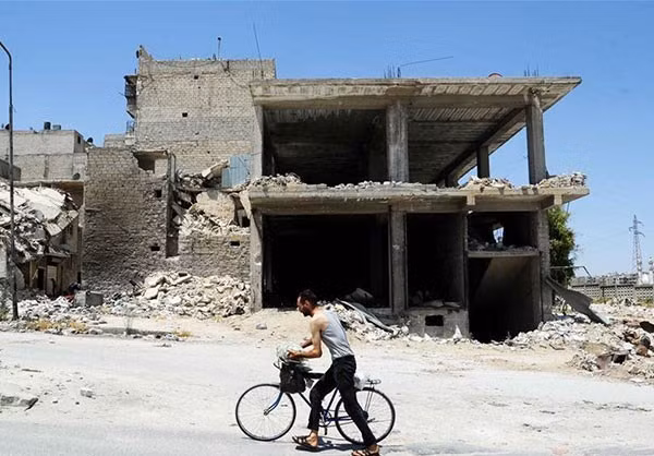 Người đàn ông dắt xe đi qua tòa nhà đổ nát ở thành phố lớn nhất Syria. Ảnh: FNA.