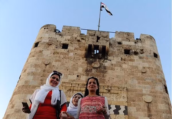 Những người phụ nữ tươi cười chụp ảnh khi lá cờ Syria tung bay ở thành phố Aleppo. Ảnh: FNA.