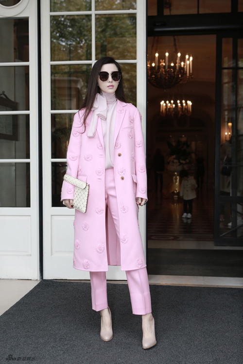Phạm Băng Băng nổi bật với cây hồng gồm áo khoác hồng dáng dài đính họa tiết hoa cúc, phối cùng áo thắt nơ hồng nhạt, giày màu be, ví cầm tay trắng.