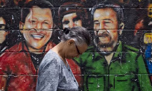 Một phụ nữ đi qua bức tranh graffiti vẽ cố Tổng thống Venezuela Hugo Chavez (trái) và lãnh tụ Fidel Castro (phải).