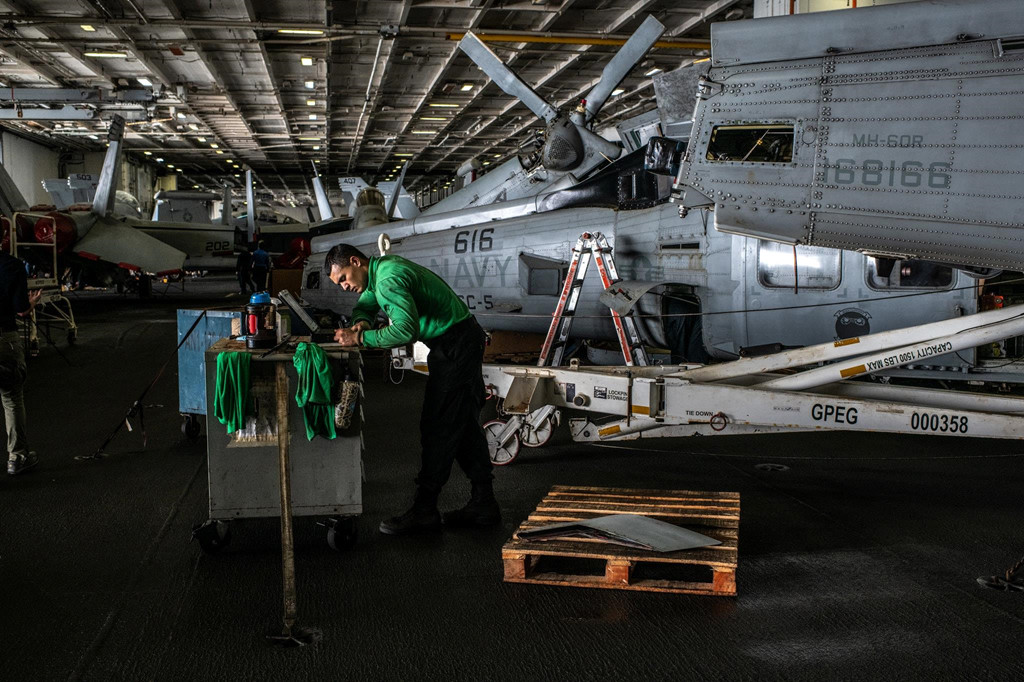 Kỹ thuật viên bảo trì trực thăng bên trong nhà chứa máy bay. Tuy tàu sân bay Lincoln ở cách Iran gần 1.000 km, các quan chức Hải quân Mỹ khẳng định rằng họ có thể đáp ứng mọi nhiệm vụ trên Vịnh Ba Tư hoặc eo biển Hormuz từ biển Arab. Ảnh: New York Times.