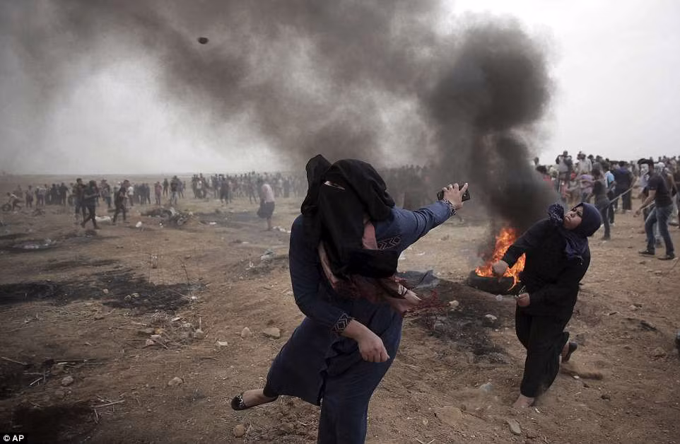 Những người phụ nữ Palestine ném đá về phía binh sĩ Israel trong cuộc biểu tình ở biên giới Dải Gaza.