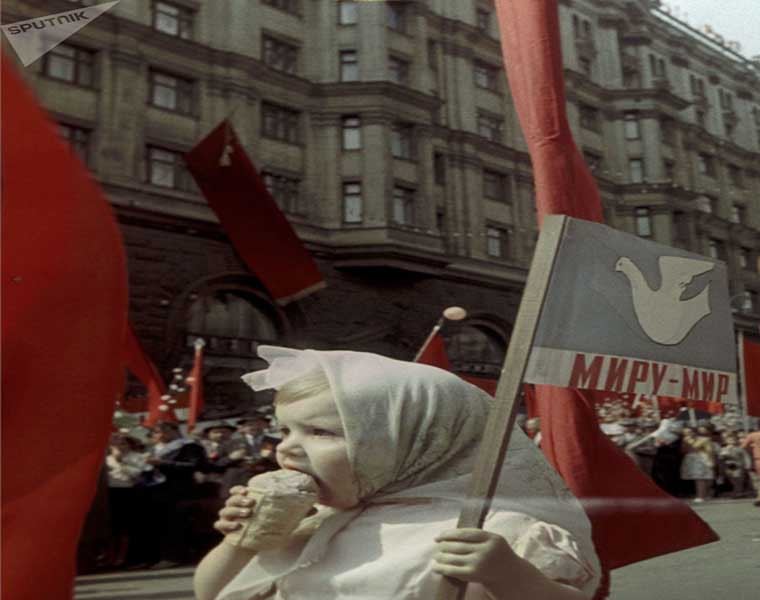Một em nhỏ vừa ăn kem vừa cầm cờ theo dõi cuộc diễu hành ở thủ đô Moscow năm 1964.