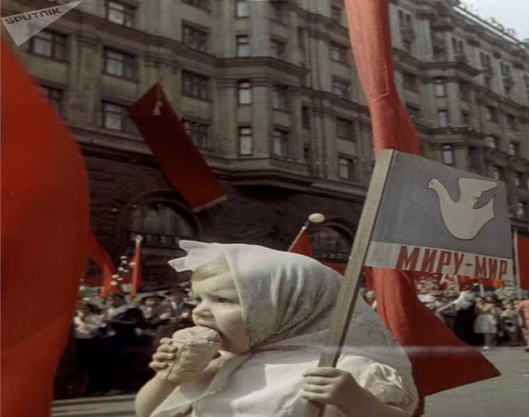 Một em nhỏ vừa ăn kem vừa cầm cờ theo dõi cuộc diễu hành ở thủ đô Moscow năm 1964.