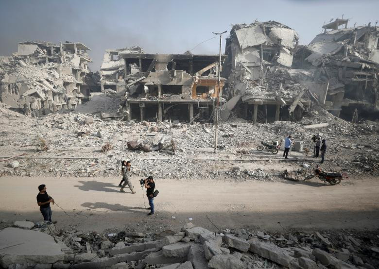 Mọi người đi qua những tòa nhà đổ nát ở al-Hajar al-Aswad ngày 21/5.