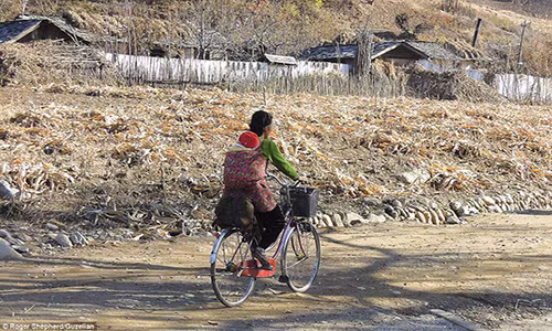 Người phụ nữ chở con bằng xe đạp trên con đường làng ở Sinyang, tỉnh Phyongannam-do, Triều Tiên.