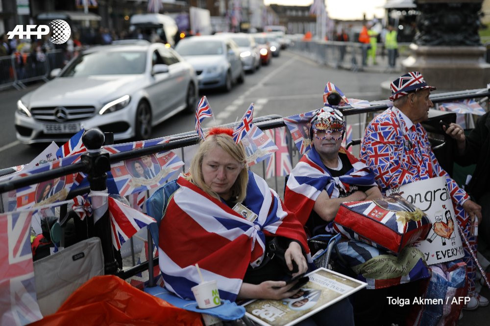 Nhiều khách du lịch đến Anh cũng đổ về địa điểm xung quanh Lâu đài Windsor. Giới chức cho hay hệ thống đường sắt sẽ phải chịu áp lực lớn. Sân bay Heathrow báo cáo lượng hành khách tăng 15% so với tuần trước. Trong ảnh, người dân sẵn sàng đón cặp đôi Hoàng gia với cờ, các đồ lưu niệm và biểu ngữ. Ảnh: AFP.