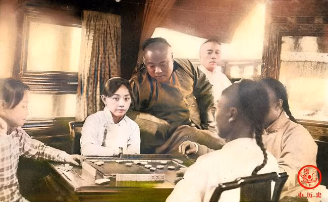 Một nhóm thanh niên chơi mạt chược, trong đám đông ấy nổi bật là người phụ nữ có vẻ đẹp sắc sảo.