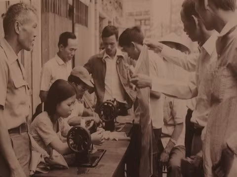 Một phụ nữ cùng nhiều người ở Đà Nẵng mang máy may ra hè phố để may cờ cho người dân xuống đường ăn mừng ngày hai miền thống nhất, đất nước độc lập 30/4/1975.